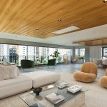 Sala de estar espaçosa em um imóvel de alto padrão, com móveis modernos, teto de madeira e ampla varanda com vista para a cidade. O ambiente integra conforto e sofisticação, ideal para viver.